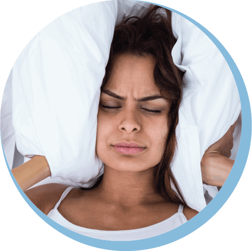 a irritated woman covering ears with pillow to block snoring sound while lying on bed