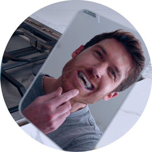 round image of man looking at his mouth in the mirror after molding the ZQuiet Advance mouthpiece