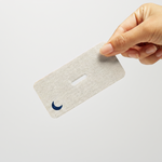 Hand holding a single ZQuiet Breathe Mouth Tape strip with a blue crescent moon symbol on a white background