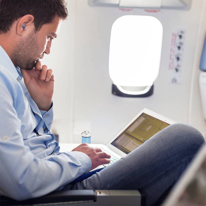 side view of a man on a plane wearing ZQuiet earplugs while working on a laptop